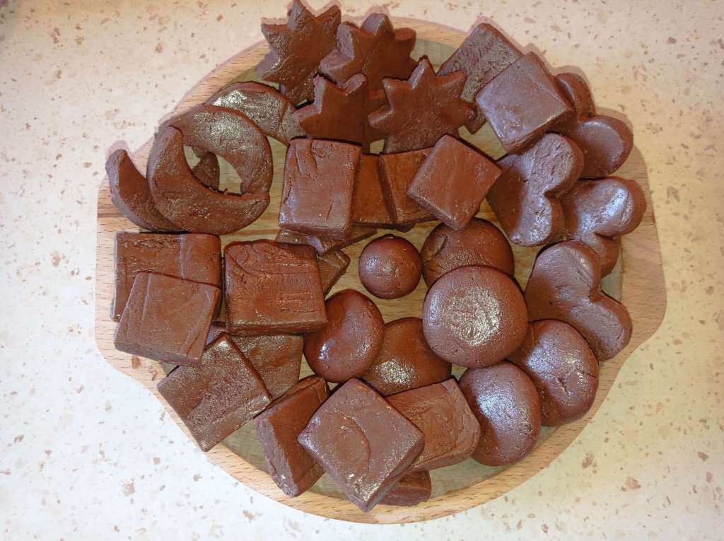 A wooden plate filled with homemade chocolate fudge in various shapes, showcasing its rich texture and deep brown color