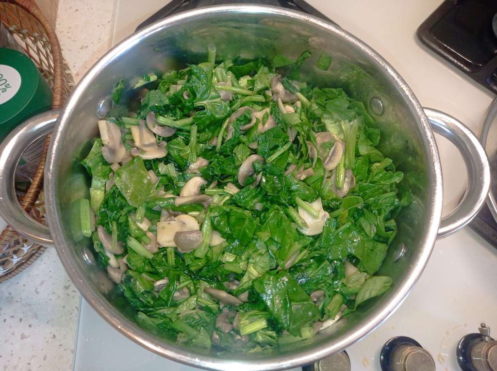A stainless steel pot containing sautéed spinach and mushrooms after 7 minutes of cooking, with visible reduction in volume and released juices