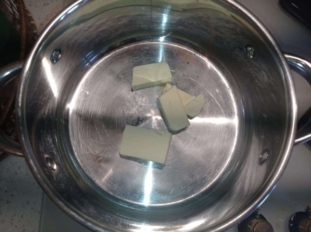 A stainless steel pot on a stove burner with butter melting inside