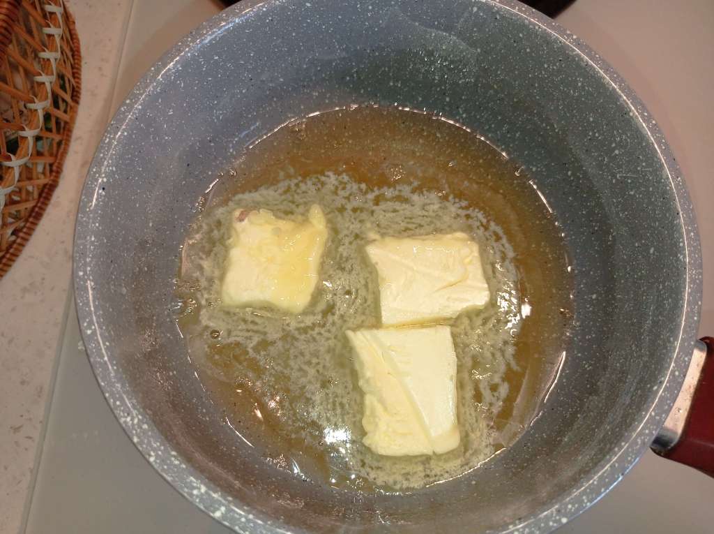 Close-up of sugar syrup heating in a small pot on the stove with three pieces of butter added.
