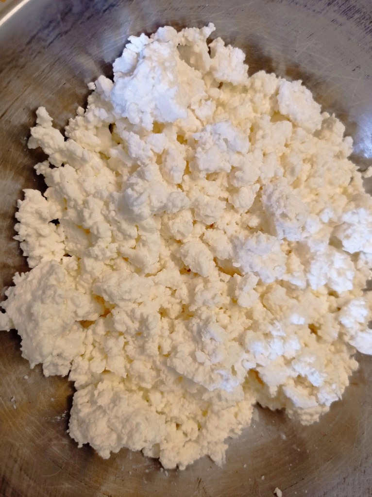Close-up of crumbled fresh cottage cheese in a metal bowl, ideal for Romanian Pasca filling
