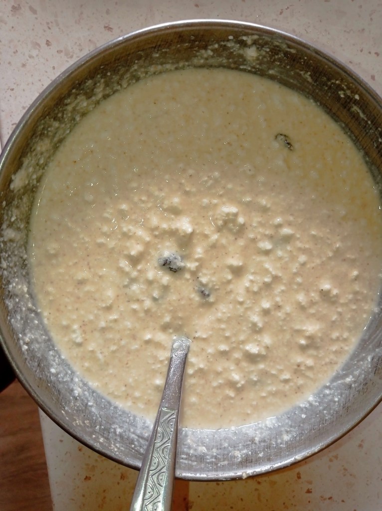 Pasca filling mixture in a metal bowl, made with cottage cheese, eggs, sour cream, sugar, and raisins