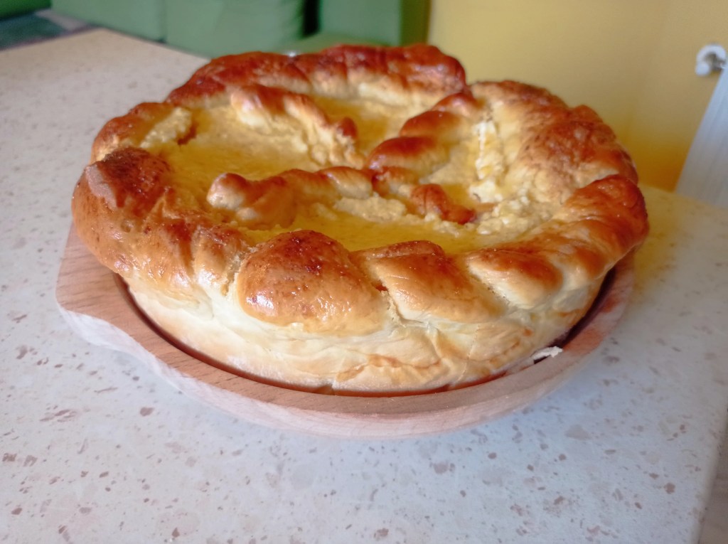 Golden-brown Pasca seen from the side, showing its tall braided crust and creamy baked filling