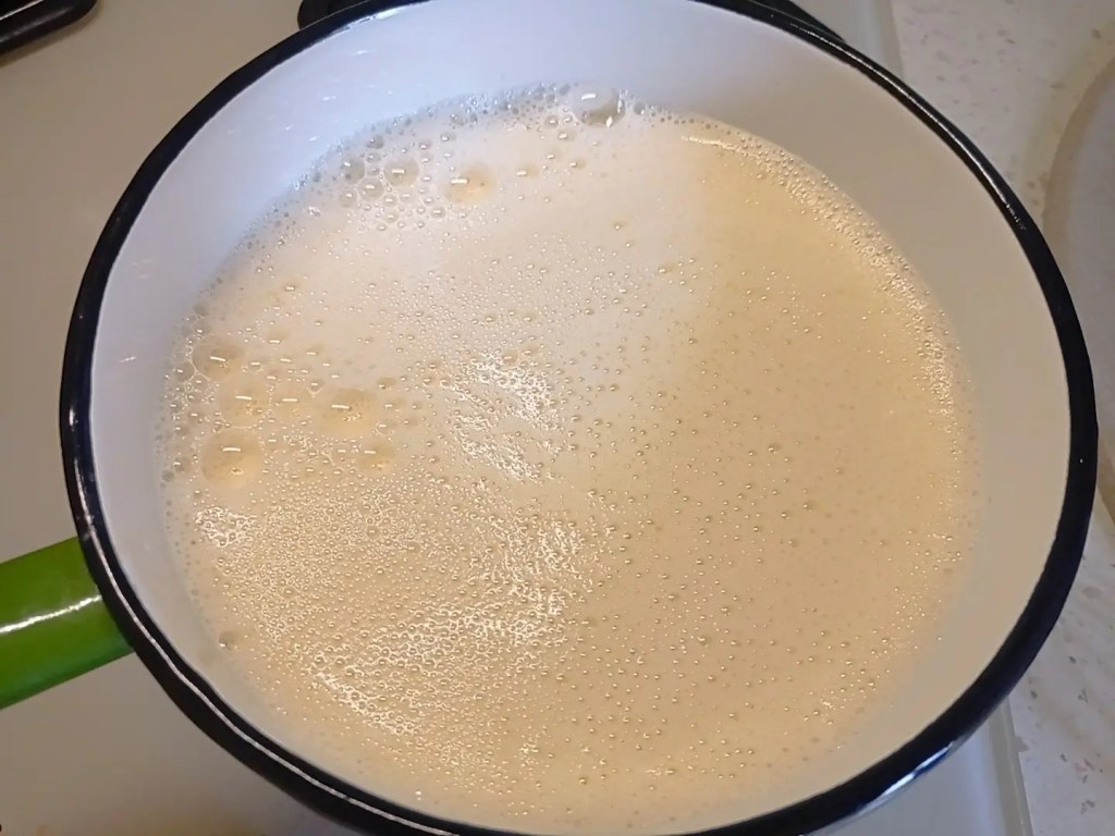 Vanilla custard base with lactose-free milk, yolks, and sugar heating in a white saucepan