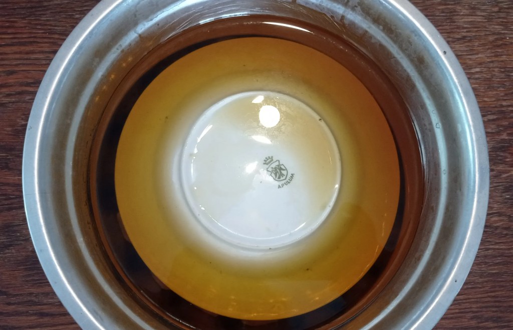 Bowl of green walnuts covered with a plate, showing darkened water after overnight refrigeration.