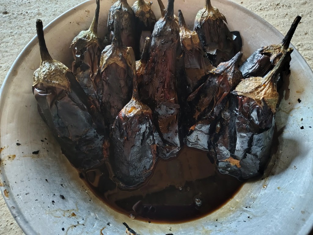Roasted eggplants placed upright in a bowl, draining the excess dark liquid after cooking