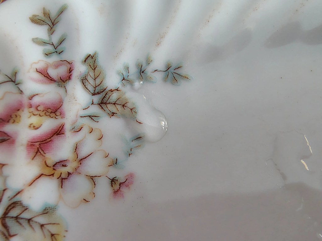 A drop of strawberry syrup on a floral plate, showing the traditional Romanian “room temp plate” test to check syrup consistency for whole-fruit strawberry preserve.